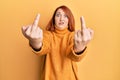 Beautiful redhead woman showing middle finger doing bad gesture in shock face, looking skeptical and sarcastic, surprised with