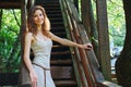 Beautiful redhead woman stands on the wooden stairs of an old house. Smiling young woman in summer dress Royalty Free Stock Photo