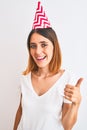 Beautiful redhead woman wearing birthday cap over isolated background doing happy thumbs up gesture with hand