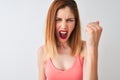 Beautiful redhead woman wearing casual pink t-shirt standing over isolated white background annoyed and frustrated shouting with Royalty Free Stock Photo