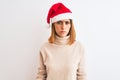 Beautiful redhead woman wearing christmas hat over background skeptic and nervous, frowning upset because of problem