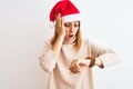 Beautiful redhead woman wearing christmas hat over isolated background Looking at the watch time worried, afraid of getting late