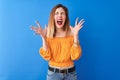 Beautiful redhead woman wearing orange casual t-shirt standing over isolated blue background celebrating mad and crazy for success