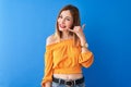 Beautiful redhead woman wearing orange casual t-shirt standing over isolated blue background smiling doing phone gesture with hand Royalty Free Stock Photo