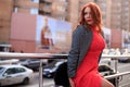 Beautiful redhead woman wearing red dress and stylish coat on city street. loneliness and depression concept Royalty Free Stock Photo