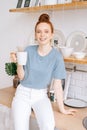 Beautiful redhead young woman holding cup of hot coffee while standing in kitchen room. Royalty Free Stock Photo