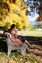 redhead woman in checked coat and black beret reading book on bench, resting in autumn park at sunny day Royalty Free Stock Photo
