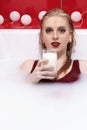 Beautiful redhead  young woman with red lips lying in milk bath is holding glass of milk Royalty Free Stock Photo