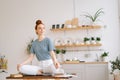 Beautiful redhead young woman sitting in lotus pose at the desk and looking away. Royalty Free Stock Photo