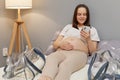 Beautiful relaxed pregnant woman lying on bed touching her bare belly using smartphone scrolling online browsing internet web Royalty Free Stock Photo