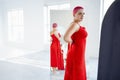 Beautiful relaxed woman in red long dress and red shot hair looking to the mirro