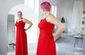 Beautiful relaxed woman in red long dress and red shot hair hlooking to the mirro