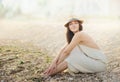 Beautiful relaxing woman sitting on a sand sea beach dressed in white dress.