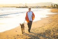 Happy attractive senior woman with her german shepard dog walking on the beach at autumn sunset Royalty Free Stock Photo