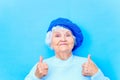 beautiful retired woman in blue beret and warm pullover looking at camera and smile in blue wall background in studio