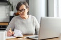 Beautiful retirement woman using a laptop sitting at the desk in the kitchen