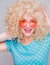 Beautiful retro-style blonde girl with voluminous curly hairstyle, in a blue polka-dot blouse and pink glasses on a gray Royalty Free Stock Photo