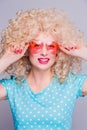 Beautiful retro-style blonde girl with voluminous curly hairstyle, in a blue polka-dot blouse and pink glasses on a gray Royalty Free Stock Photo