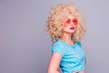 Beautiful retro-style blonde girl with voluminous curly hairstyle, in a blue polka-dot blouse and pink glasses on a gray Royalty Free Stock Photo