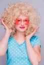 Beautiful retro-style blonde girl with voluminous curly hairstyle, in a blue polka-dot blouse and pink glasses on a gray Royalty Free Stock Photo