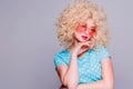 Beautiful retro-style blonde girl with voluminous curly hairstyle, in a blue polka-dot blouse and pink glasses on a gray Royalty Free Stock Photo