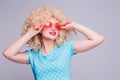 Beautiful retro-style blonde girl with voluminous curly hairstyle, in a blue polka-dot blouse and pink glasses on a gray Royalty Free Stock Photo