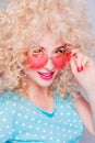 Beautiful retro-style blonde girl with voluminous curly hairstyle, in a blue polka-dot blouse and pink glasses on a gray Royalty Free Stock Photo