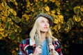 Beautiful romantic blonde girl standing at fall yellow autumnal leaves and looks dreamy. Beautiful femme wearing plaid Royalty Free Stock Photo