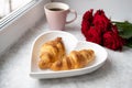 Beautiful romantic breakfast.French croissants on white heart-shaped plate , roses and cup of coffee on windowsill Royalty Free Stock Photo