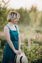 Beautiful romantic girl blonde in a dress in a field of purple flowers of lupins at dawn holds a hat in her hands Royalty Free Stock Photo