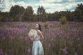Beautiful romantic girl in a delicate dress with a hat sits in a flower field of purple lupine flowers. Soft selective focus