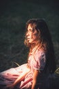 Beautiful romantic girl in vintage dress on sunny meadow. Side view dreamy young woman with curly hair sitting on grass