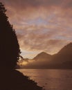 Beautiful romantic sunset golden hour landscape with foggy mountains, a lake and a dark forest with pink and orange sky Royalty Free Stock Photo