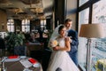 Beautiful, romantic newlyweds posing near window in luxury wedding hall before the celebration