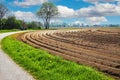 Beautiful rural dutch farm landscape, freshly tilled plowed cropland field, symmetrical curved arable furrows, empty cycle path -