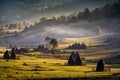 Beautiful rural mountain landscape in the morning light with fog, old houses and haystacks