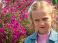 Beautiful sad blond little girl smelling flower and feeling upset. Kids pollen allergy. Sick child grimaces and sneezes Royalty Free Stock Photo