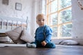 Beautiful sad blue-eyed baby sitting on a wooden floor and looking at the camera Royalty Free Stock Photo