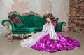 Beautiful sad crying woman in fantasy white and purple rococo style medieval dress sitting on the floor near sofa Royalty Free Stock Photo