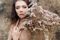 Beautiful sad cute attractive woman in a beige sweater wide in a field of dry grass in autumn cold overcast day, photo of beige