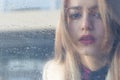 Beautiful sad girl with big eyes in a coat is behind wet glass Royalty Free Stock Photo
