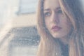 Beautiful sad girl with big eyes in a coat is behind wet glass Royalty Free Stock Photo