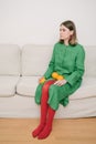 Beautiful Sad girl in green dress and red tights sitting on beige sofa. Royalty Free Stock Photo