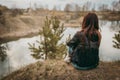 Beautiful sad girl sitting on the lake in jeans, looking into the distance and thinking about the meaning of life. The concept of