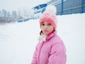 Beautiful sad girl 7 years old on a background of snow. A pink knitted hat and a pink winter warm jacket are worn by the child. Royalty Free Stock Photo