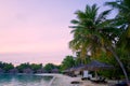 Beautiful sand beach with lush palm trees and thatch umbrellas with sunbeds during a sunrise