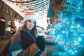 Beautiful Santa girl stands with a cup of coffee in her hand near a Christmas tree on street background decorated with Christmas Royalty Free Stock Photo