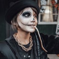 Beautiful scary little girl celebrating halloween, chewing gummy worm. Terrifying face makeup and witch costume