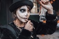 Beautiful scary little girl celebrating halloween, chewing gummy worm. Terrifying face makeup and witch costume