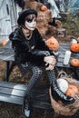 Beautiful scary little girl celebrating halloween. Terrifying black, white half-face makeup and witch costume